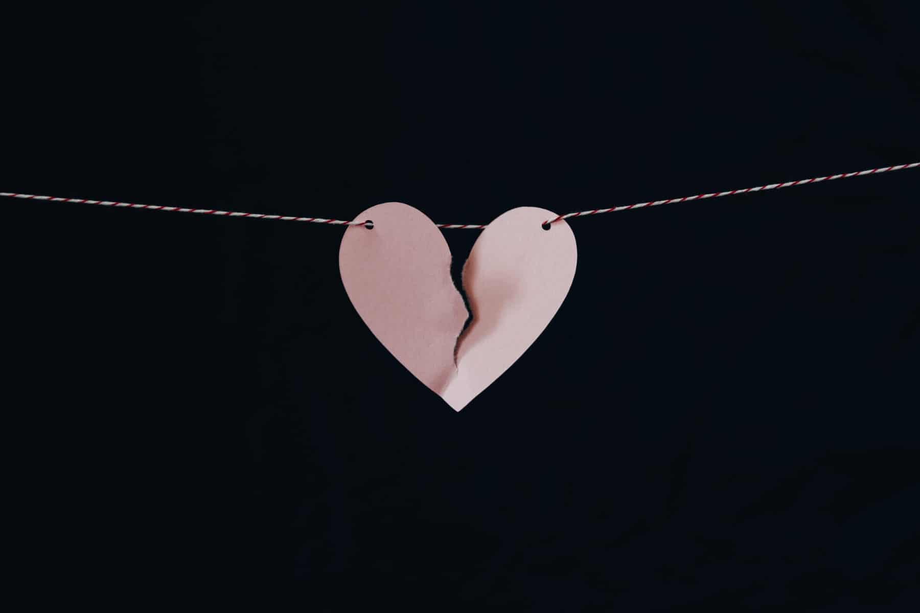 self sabotaging behaviours. Pink ripped paper heart on black background.