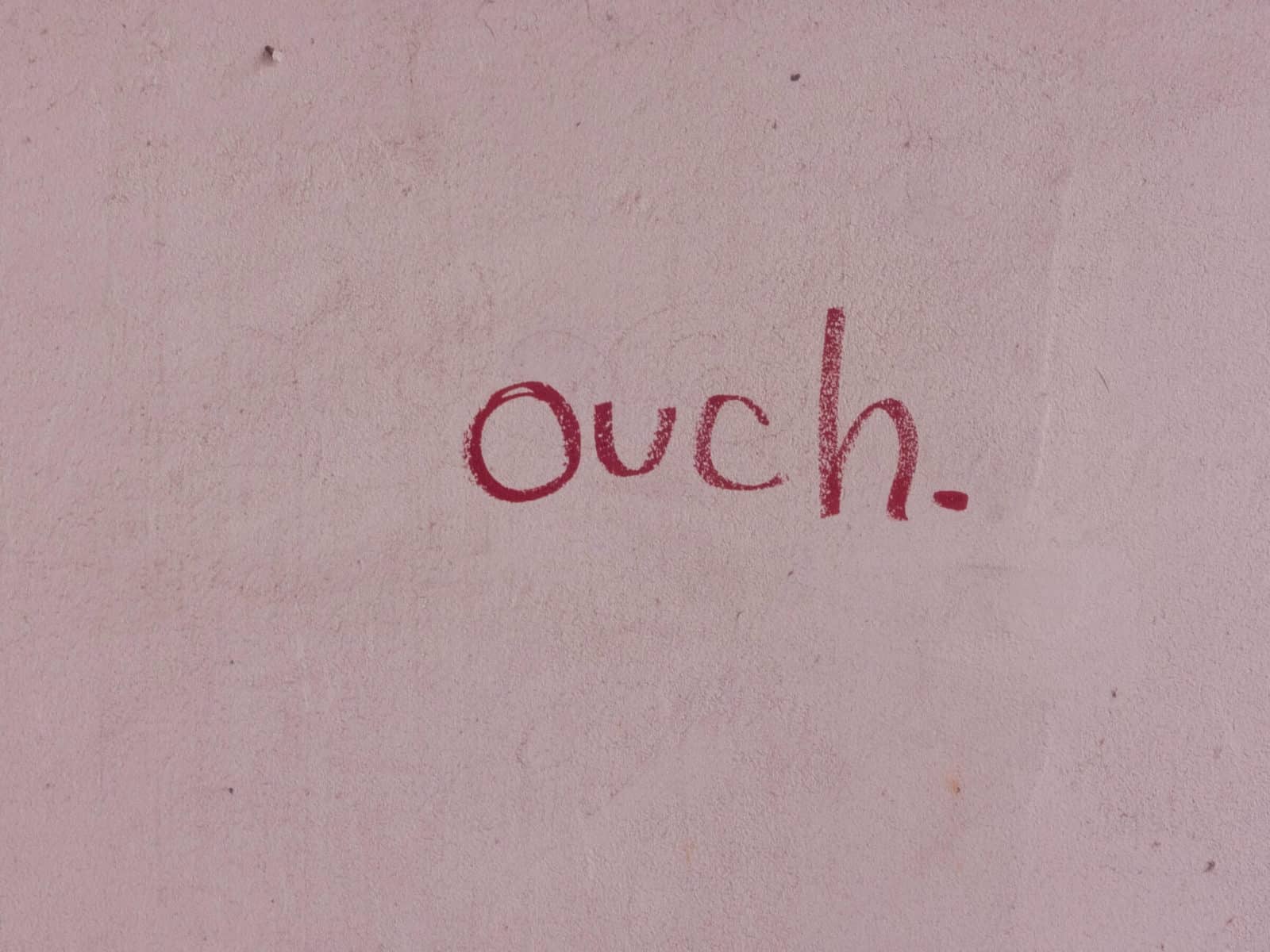 self sabotaging behaviours. Red crayon spells 'ouch' on blush pink wall.